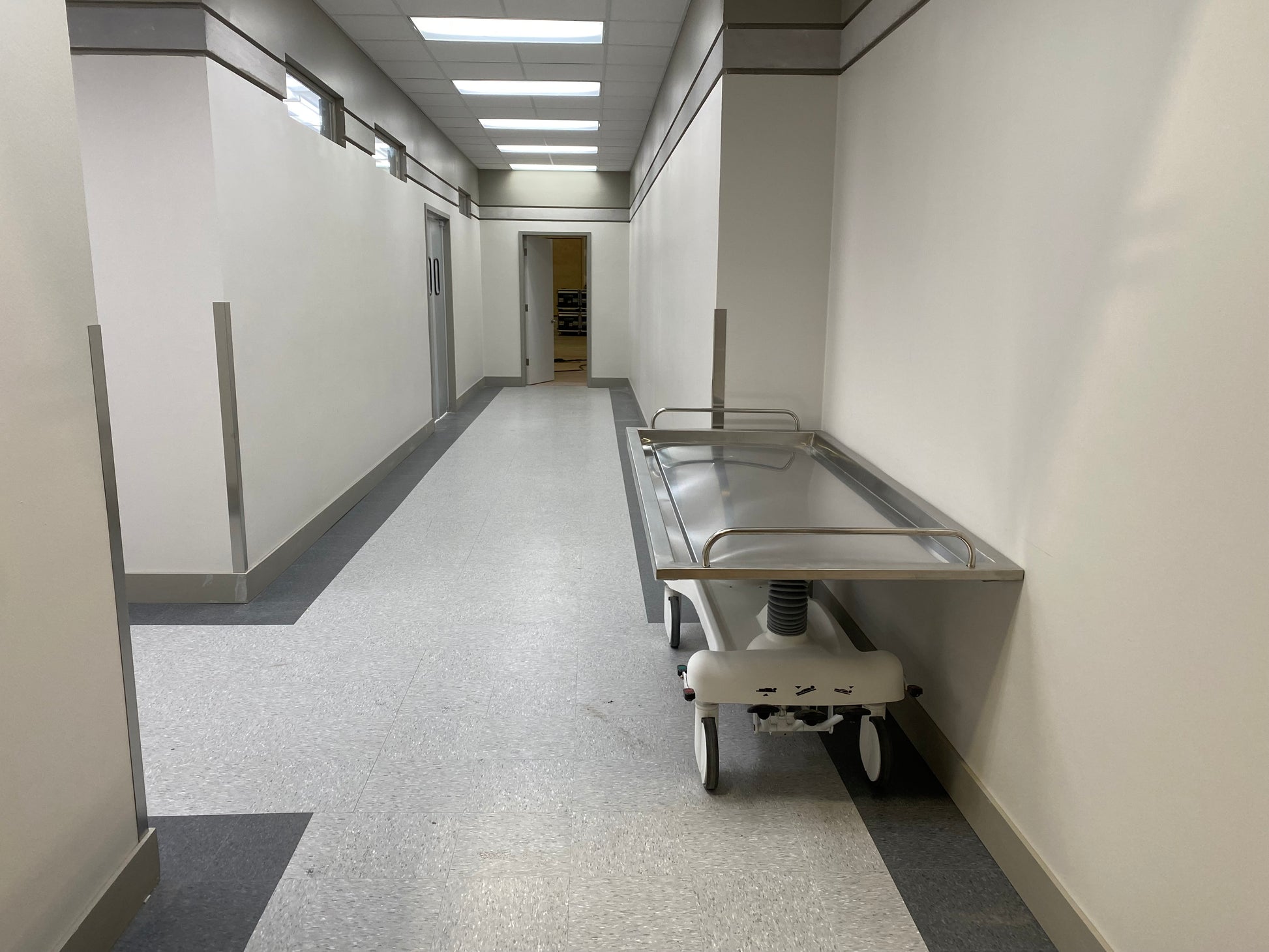 Oversized hydraulic embalming table stainless steel convex top and perimeter drainage trough in a funeral home prep room